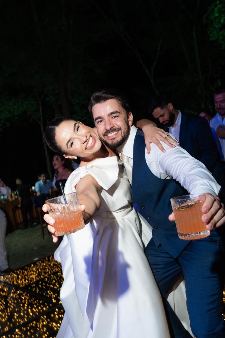 Noivos sorrindo segurando drinks em festa de casamento